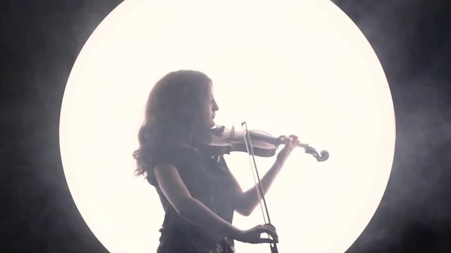 Silhouette of a girl-musician. The violinist plays the violin in smoke against a white circle.