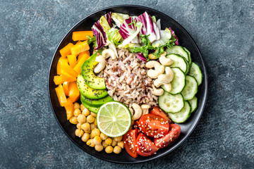 Vegetarian salad Buddha bowl dish with brown rice, avocado, pepper, tomato, cucumber, chickpea, chia seeds, fresh lettuce salad and cashew nuts. Healthy eating trend, superfood. Top view