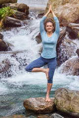 Woman in yoga asana Vrikshasana tree pose at waterfall outdoors