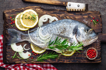 Fresh fish dorado with ingredients for cooking on wooden board. Raw sea bream or dorada fish on dark vintage metal background. Dietary food. Top view