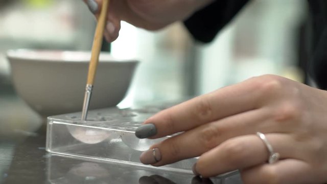 Close up of baking dish is being greased with butter on the kitchen. Femle confectioner with beautiful manicure and silver ring on the finger is using brush to prepare plastic forms for cooking