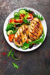 Grilled chicken breast. Fried chicken fillet and fresh vegetable salad of tomatoes, cucumbers and arugula leaves. Chicken meat with salad. Healthy food. Flat lay. Top view. Dark background