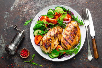 Grilled chicken breast. Fried chicken fillet and fresh vegetable salad of tomatoes, cucumbers and arugula leaves. Chicken meat with salad. Healthy food. Flat lay. Top view. Dark background