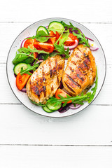Grilled chicken breast. Fried chicken fillet and fresh vegetable salad of tomatoes, cucumbers and arugula leaves. Chicken meat salad. Healthy food. Flat lay. Top view. White background