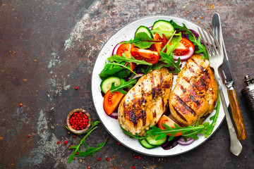 Grilled chicken breast. Fried chicken fillet and fresh vegetable salad of tomatoes, cucumbers and arugula leaves. Chicken meat with salad. Healthy food. Flat lay. Top view. Dark background