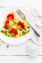 Omelet. Eggs fried. Scrambled eggs with green onion and fresh tomato. Omlette on white plate. Breakfast. Top view. White wooden background