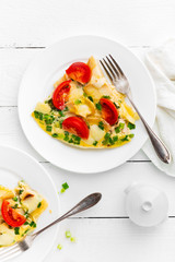 Omelet. Eggs fried. Scrambled eggs with green onion and fresh tomato. Omlette on white plate. Breakfast. Top view. White wooden background