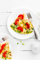 Omelet. Eggs fried. Scrambled eggs with green onion and fresh tomato. Omlette on white plate. Breakfast. Top view. White wooden background