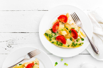 Omelet. Eggs fried. Scrambled eggs with green onion and fresh tomato. Omlette on white plate. Breakfast. Top view. White wooden background