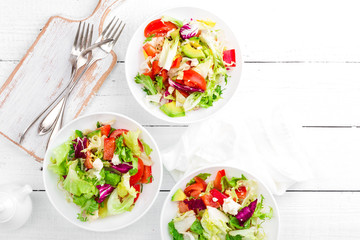 Healthy vegetable salad with fresh greens, lettuce, avocado, tomato, seet pepper and  goat cheese. Delicious and nutritious diet dish for breakfast. Salad bowls on white wooden background