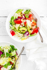 Healthy vegetable salad with fresh greens, lettuce, avocado, tomato, seet pepper and  goat cheese. Delicious and nutritious diet dish for breakfast. Salad bowls on white wooden background