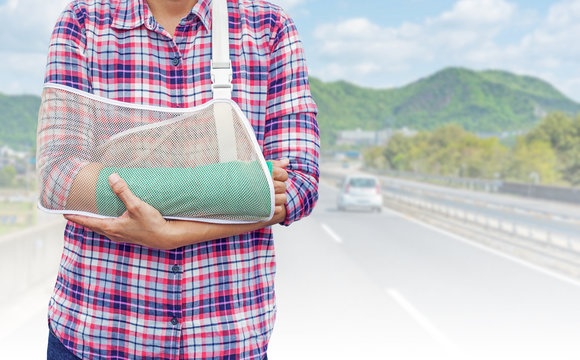 broken arm with green cast and arm sling isolated on blurred cars run on a Japanese highway with mountain background, insurance concept
