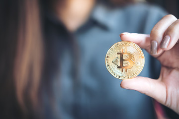 Closeup image of a business woman holding and showing a golden color bitcoin  in office