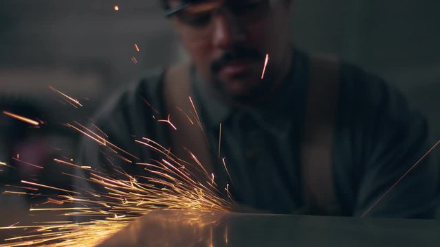 Worker using industrial grinder. Worker in garage makes work with metall and grinder. Slow motion how flying sparks
