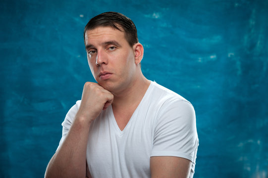 Serious and thoughtful man wearing white t-shirt posing on blue background