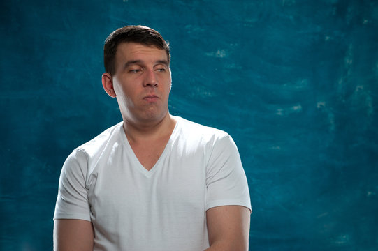Young displeased man posing on blue background. Place for text.