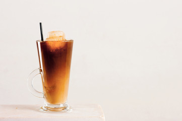 Glass of cold coffee or tea with milk and ice cubes on the white table