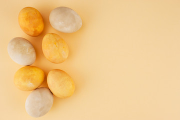 Colored yellow and beige Easter eggs on the light-yellow paper background