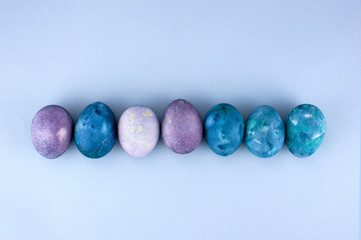 Colored blue and violet Easter eggs on the light-blue paper background