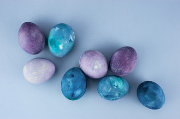 Colored blue and violet Easter eggs on the light-blue paper background