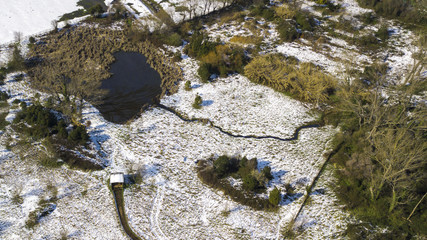 Aerial view of a small lake inside a city park. The snow covers most of the grass and forest trees....