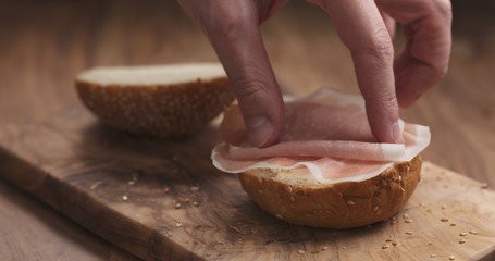 Obraz na płótnie Canvas making sandwich with prosciutto and cream cheese on wood board