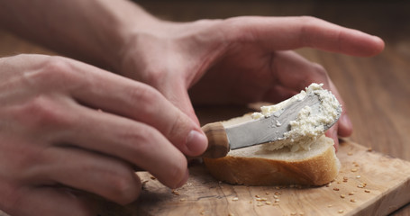 man hands spreading cream cheese on baguette slice on wood board