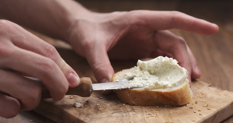 man hands spreading cream cheese on baguette slice on wood board