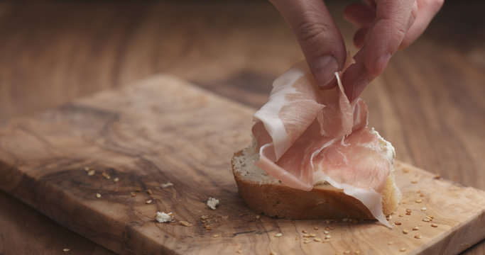 Making Prosciutto On Baguette Slice With Cream Cheese On Wood Board