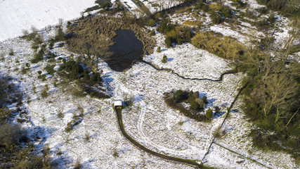 Aerial view of a small lake inside a city park. The snow covers most of the grass and forest trees....