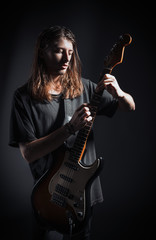 Dramatic studio portrait: handsome young man (rock musician) with long hair playing the electric guitar