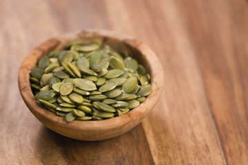 green pumkin seeds in bowl on wooden table