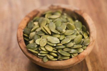 green pumkin seeds in bowl on wooden table