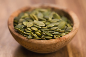 green pumkin seeds in bowl on wooden table