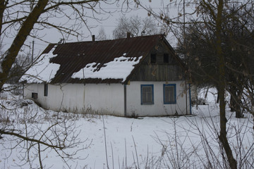 Abandoned and an old residential house against the backdrop of overgrown bushes and white snow. Ruin and vandalism.