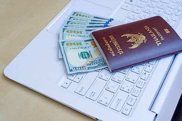 passport with US dollar on white keyborad on wood desk, travel cost concept