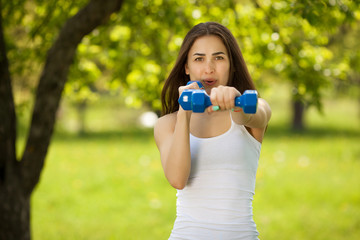 Beautiful woman exercising outdoors. Cheerful slim girl doing workout at the park in summer time