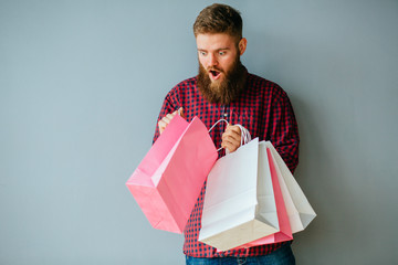 Portrait of beard man holding shopping bag on gray background. Surprise his daring woman concept.