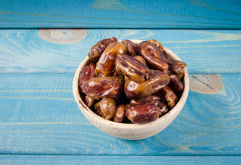 Dry dates fruit in the bowl, on the wood background.