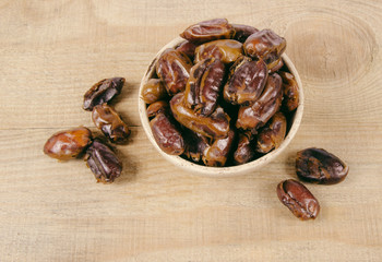 Dry dates fruit in the bowl, on the wood background.