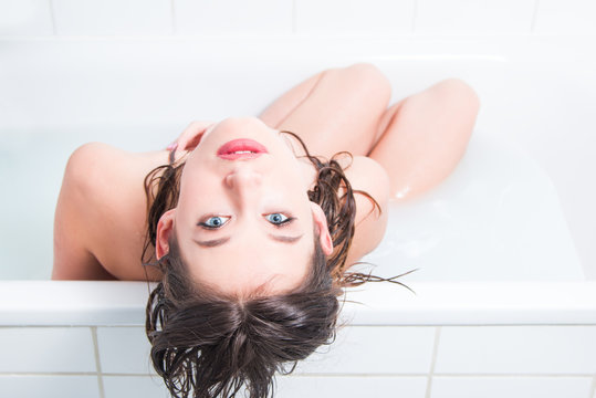 Beautiful young nude caucasian girl sitting in bath, top perspective