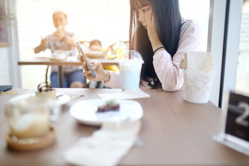 Beautiful chic cute Asian woman look down on smart phone in hand at coffee shop with blue color milk ice unicorn beverage plastic glass on wood table in alone - 194826855