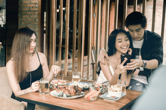 Asian single woman envious with love couple doing take selfie at restaurant.