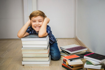 Happy little boy having fun while being surrounded with books.