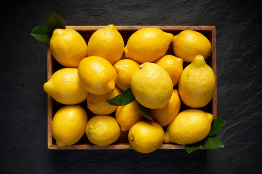 Fresh lemons in a wooden container on a black stone background, top view
