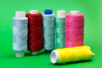 Threads of different colors on a green background. A few coils with bright multicolored threads stand on a juicy green background.