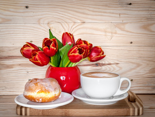 A cup of cappuccino, donut and a bouquet of tulips in a red vase. Mother's Day and Women's Day celebration
