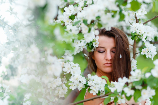Portrait of a young beautiful woman posing among blooming Apple trees. Girl with long hair posing among the flowers. Close-up with space for text.