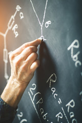 The teacher writes on a board with chalk a formula for electric current.