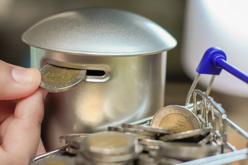 Hand picking coins from a Shopping cart into a coin bank, Saving money concept.